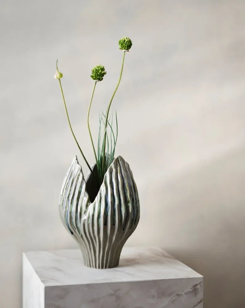 Ribbed sculptural ceramic vase with allium stems on a marble plinth